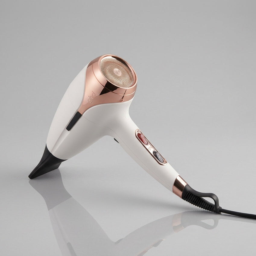 A handheld hair dryer in white and rose gold, shown at an angle on a reflective black surface against a dark gray background.
